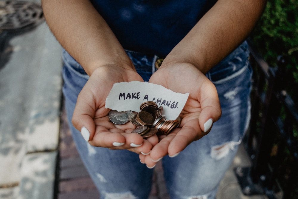 Person's cupped hands holding coin change with a note that says make a change